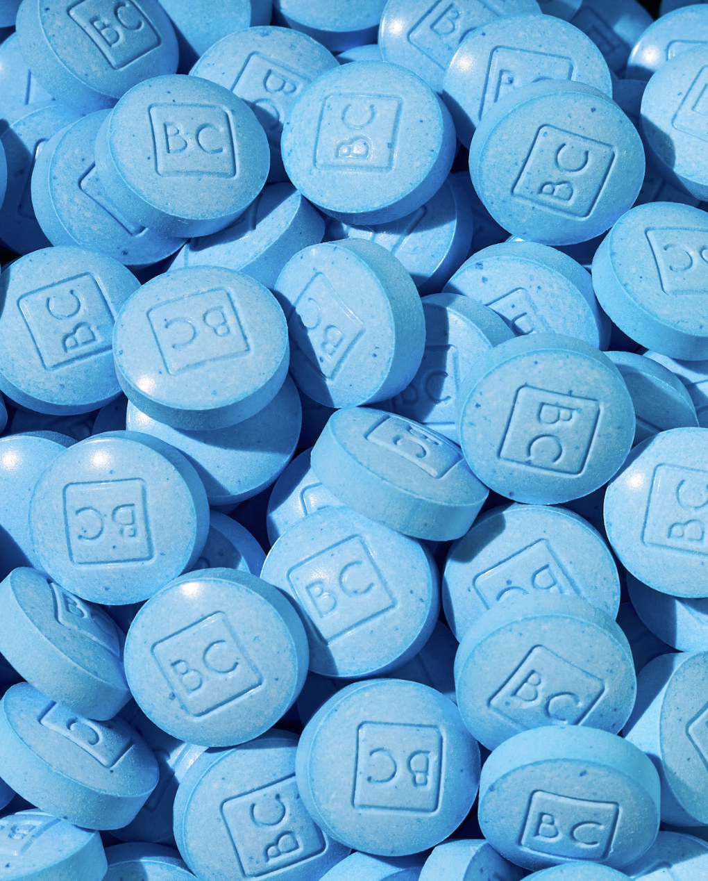 A close-up image of bluechew chewable tablets with 'BC' embossed on them, stacked closely together.