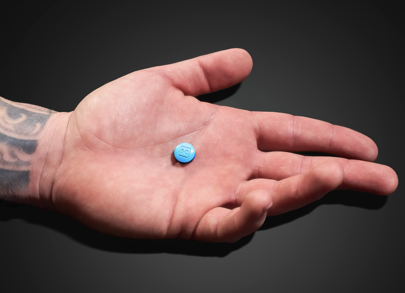 A hand holding a blue chewable bluechew tablet for erectile dysfunction against a dark background.