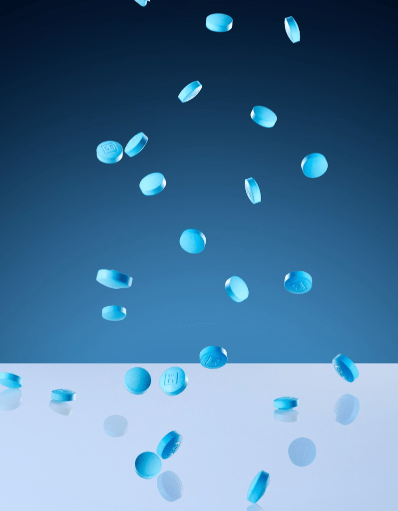Blue chewable tablets in various shapes and sizes scattered against a dark blue background.