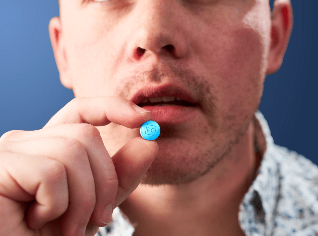A man holding a bluechew tablet labeled 'BC' close to his mouth, preparing to take it for erectile dysfunction.