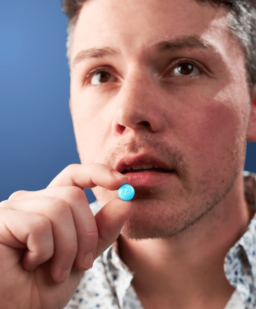 A man holding a bluechew tablet between his fingers up to his mouth ready to take his erectile dysfunction medication