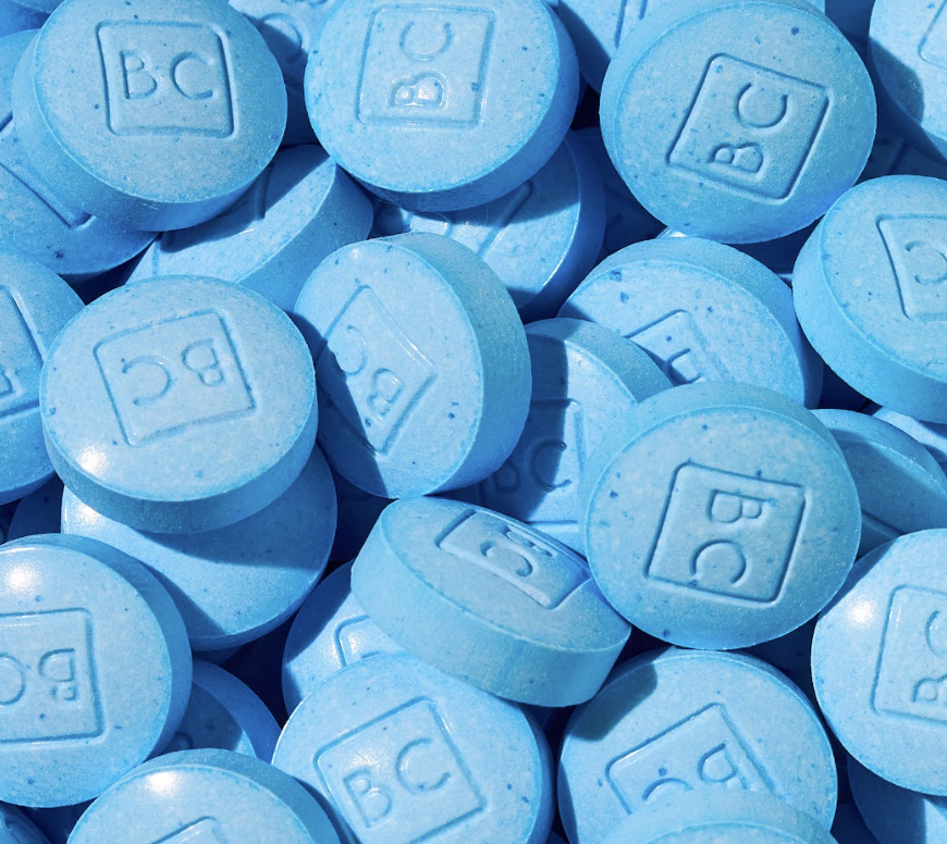 A close-up view of blue chewable tablets with 'BC' imprinted on them, scattered on a surface.
