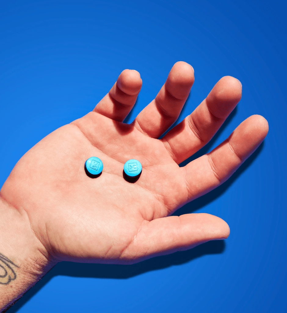 A man holding two bluechew tablets in his palm designed for enhancing erections.